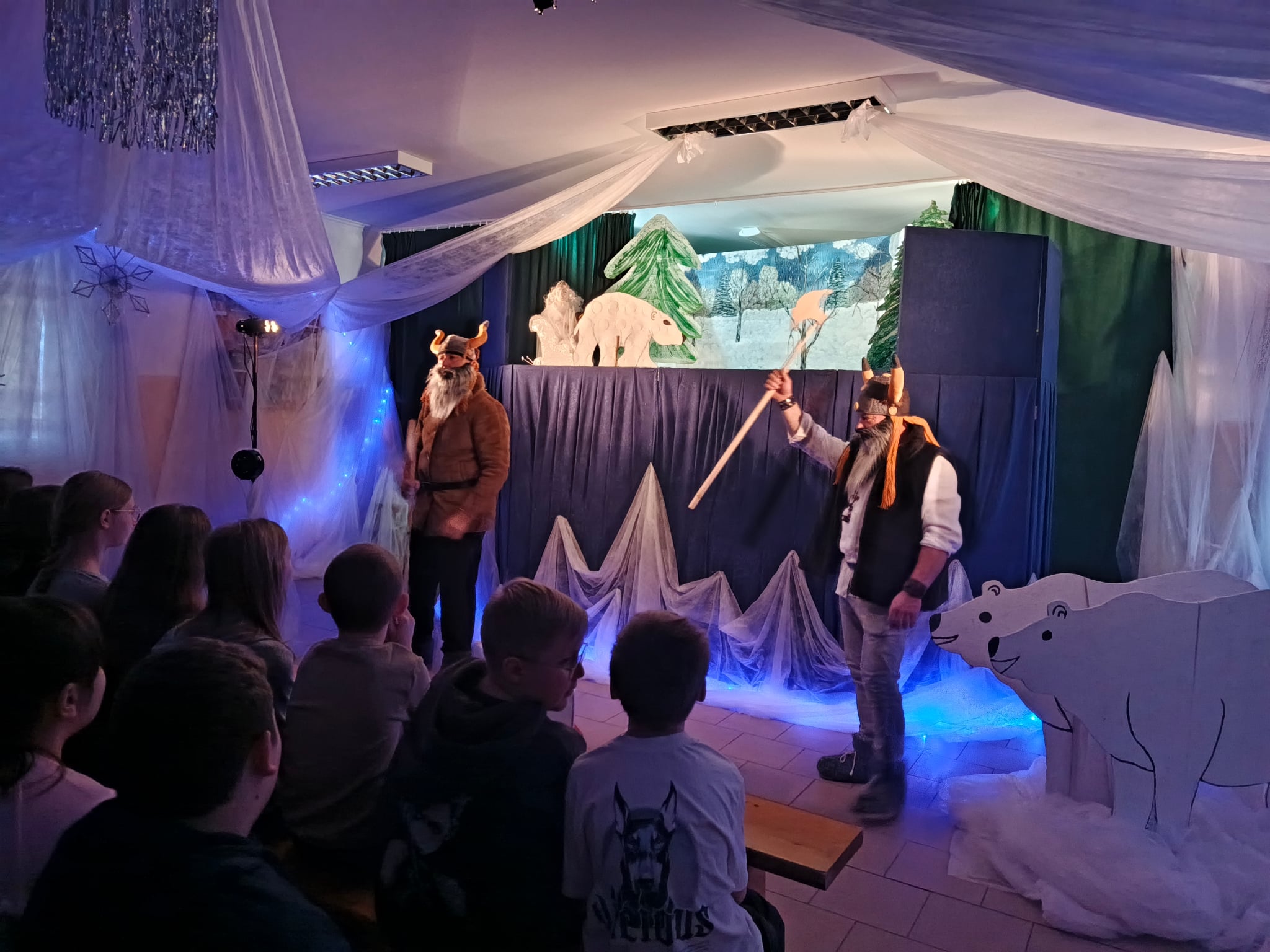 Aktorzy podczas jednej ze scen przedstawienia, w otoczeniu zimowej dekoracji i kukiełek.